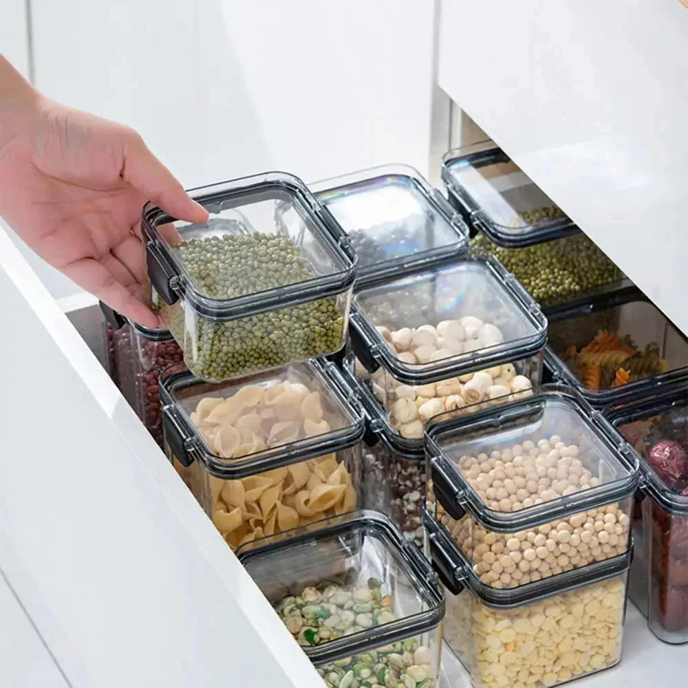 Hand organizing clear food storage containers with grains, pasta, beans in a kitchen drawer